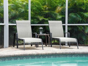Duas cadeiras de descanso com estrutura de metal e assentos de tecido cinza, localizadas perto de uma piscina com borda de azulejo.