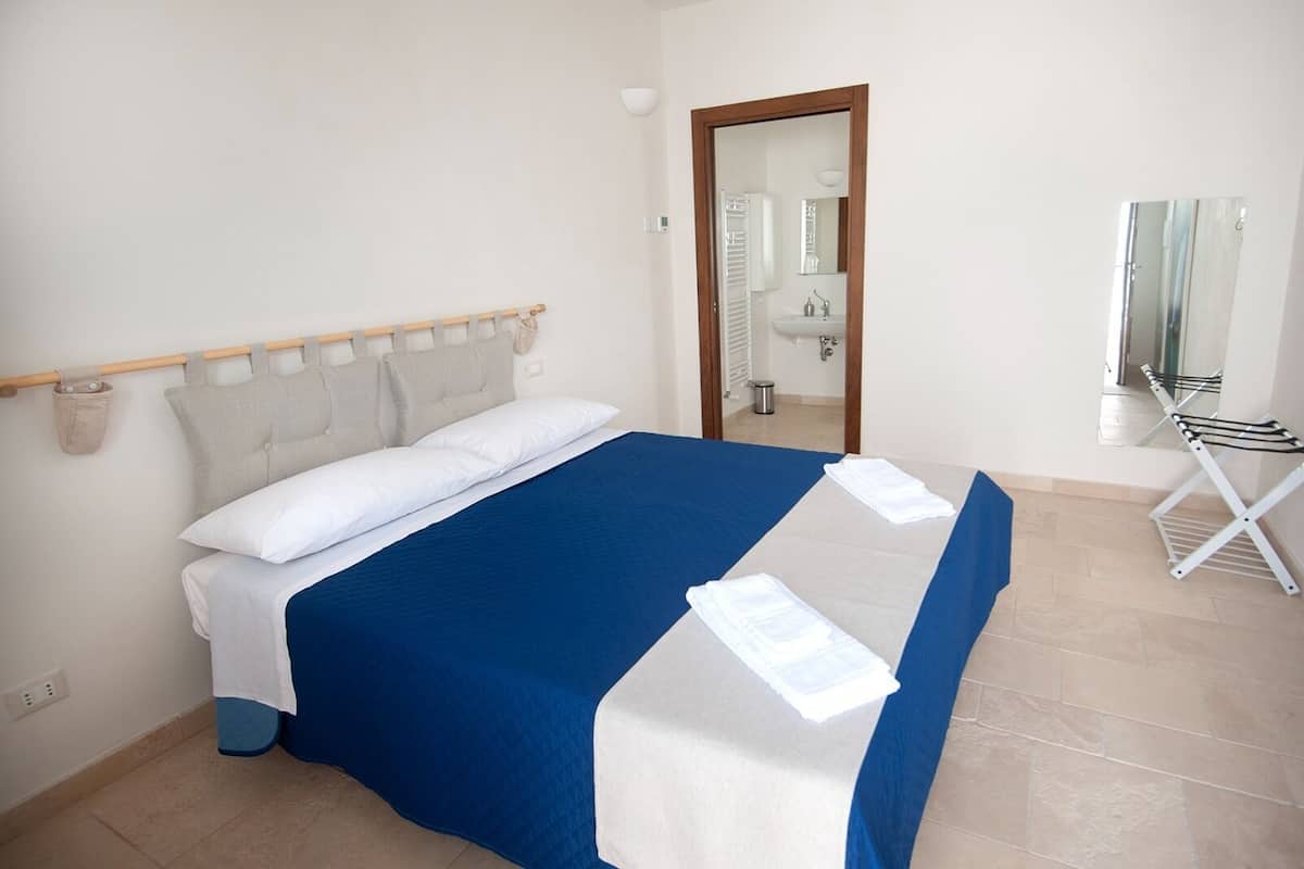 A neatly made bed with a blue and white bedspread, a wooden headboard, and a small bedside table with a lamp.