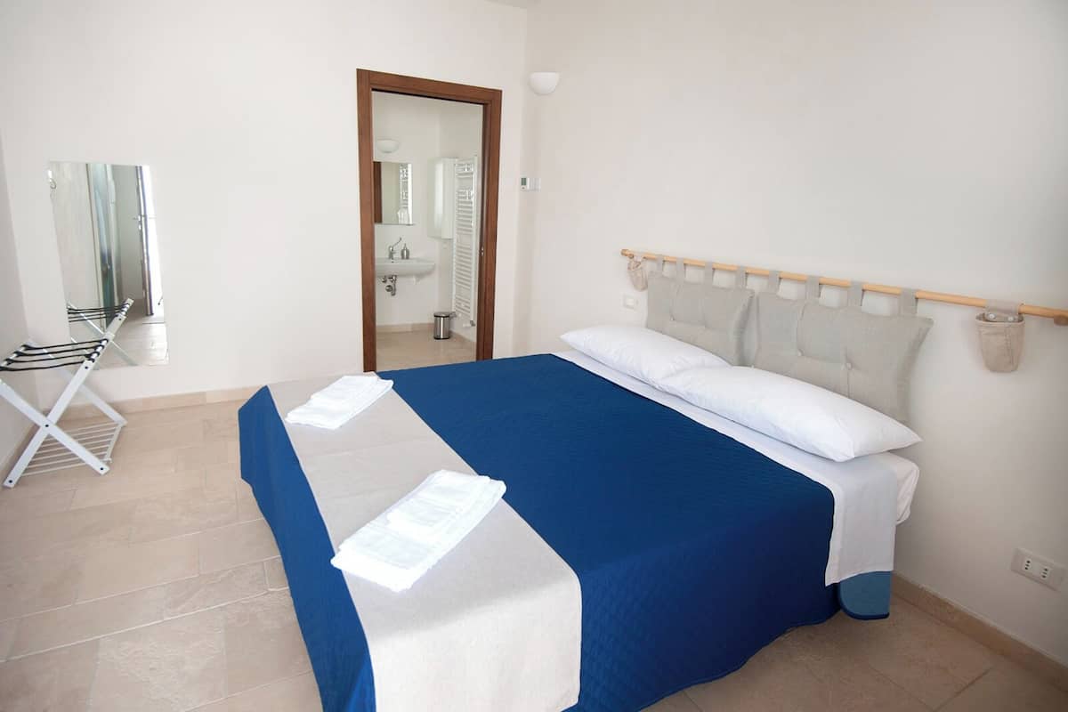 A bedroom with a bed, a mirror, a drying rack, and a view of a bathroom.