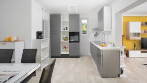 A modern kitchen with grey cabinets, a built-in oven, and a sink. There is a dining area with a table and chairs. - Romantic villa with istrian tavern (Labin)