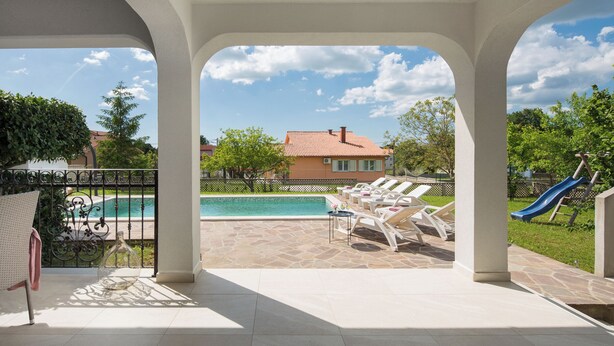 A covered outdoor area with a pool, lounge chairs, a slide, and a view of a house in the background. - Romantic villa with istrian tavern (Labin)