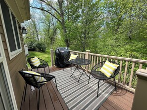 A deck with outdoor furniture, a grill, and a view of a wooded area. - Welcome to Serenity Cottage! (Galena)