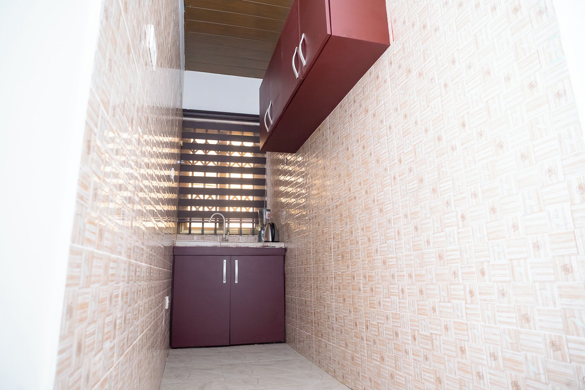 Ein schmales, geschlossenes Badezimmer mit einer gefliesten Wand, einem Holzjalousiewindfang und einem violetten Schrank mit Waschbecken.