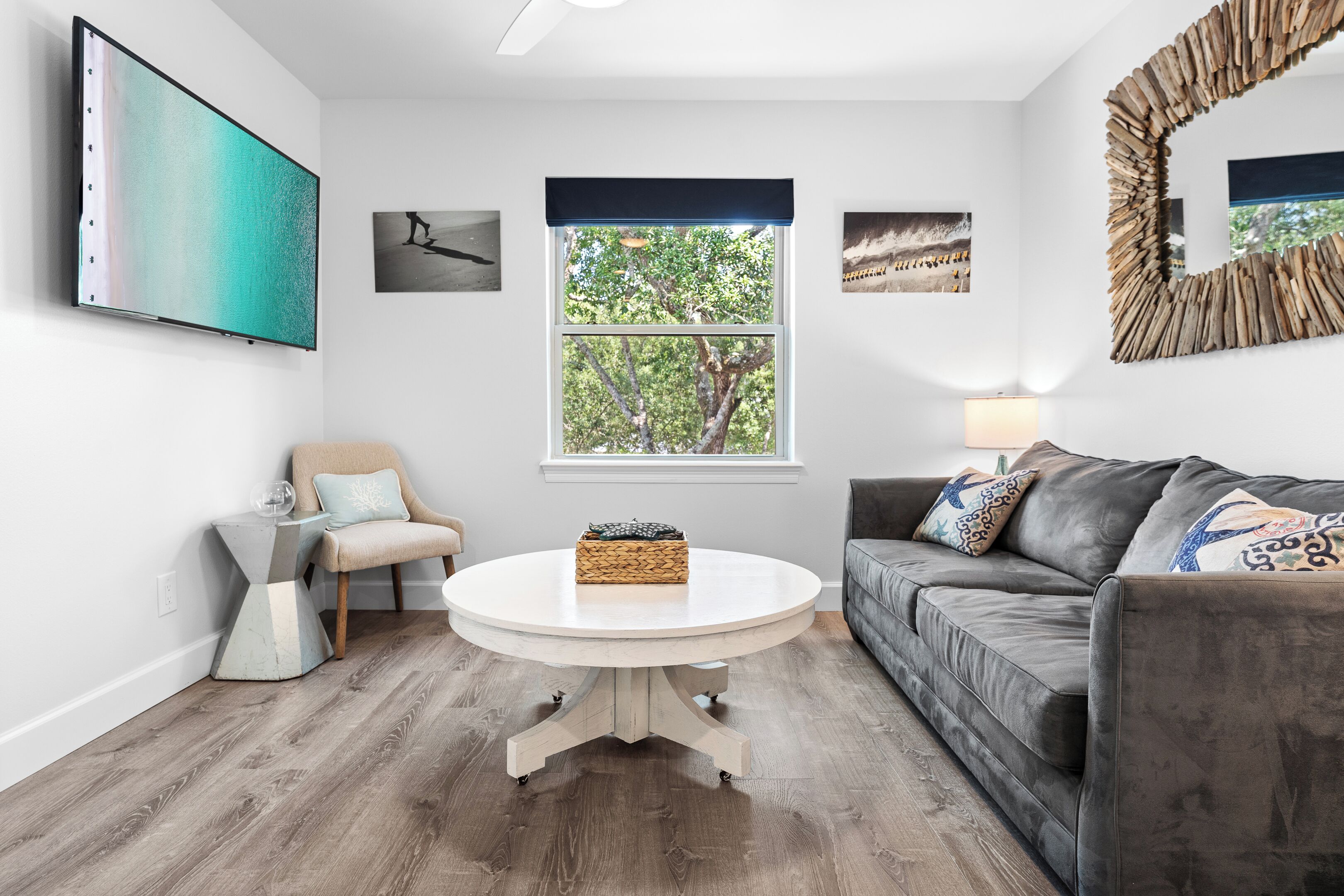 Un salon moderne avec une table ronde blanche, un canapé gris et un grand téléviseur fixé au mur.