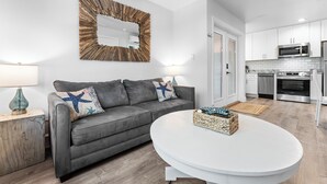 A modern living room with a grey sofa, a round white coffee table, and a kitchen in the background.