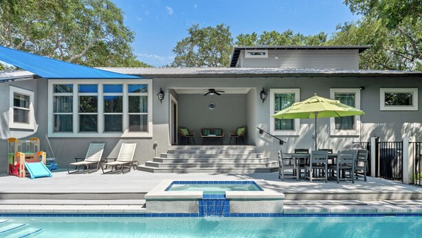 A pool area with a hot tub, lounge chairs, and a covered patio.