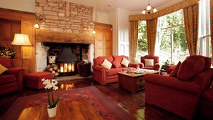 A cozy living room with a stone fireplace, red sofas, and a wooden coffee table. - Chelsea Parkfields  (Ross-on-Wye)