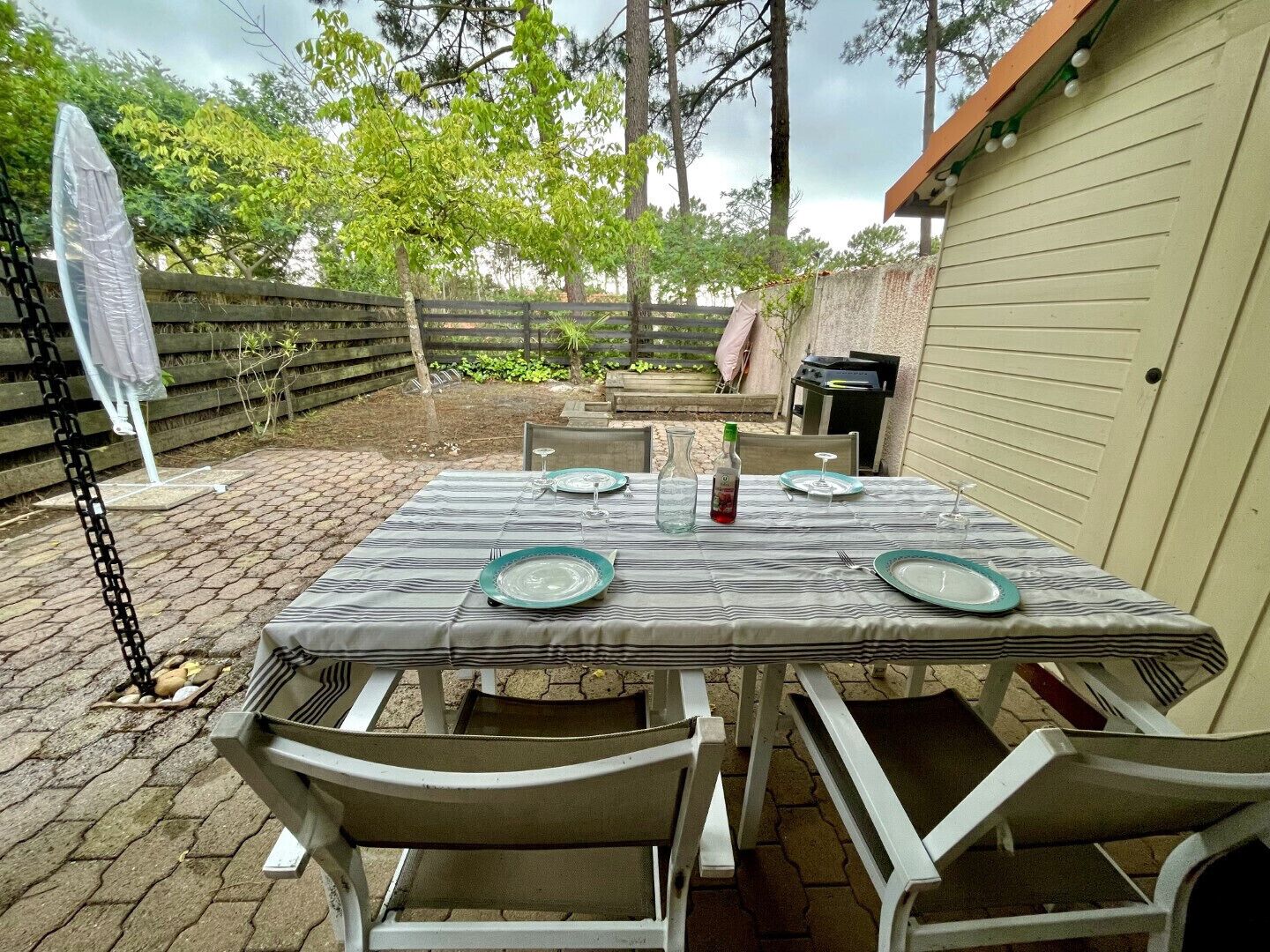 A patio with a table set for four, surrounded by chairs, a grill, and a covered area.