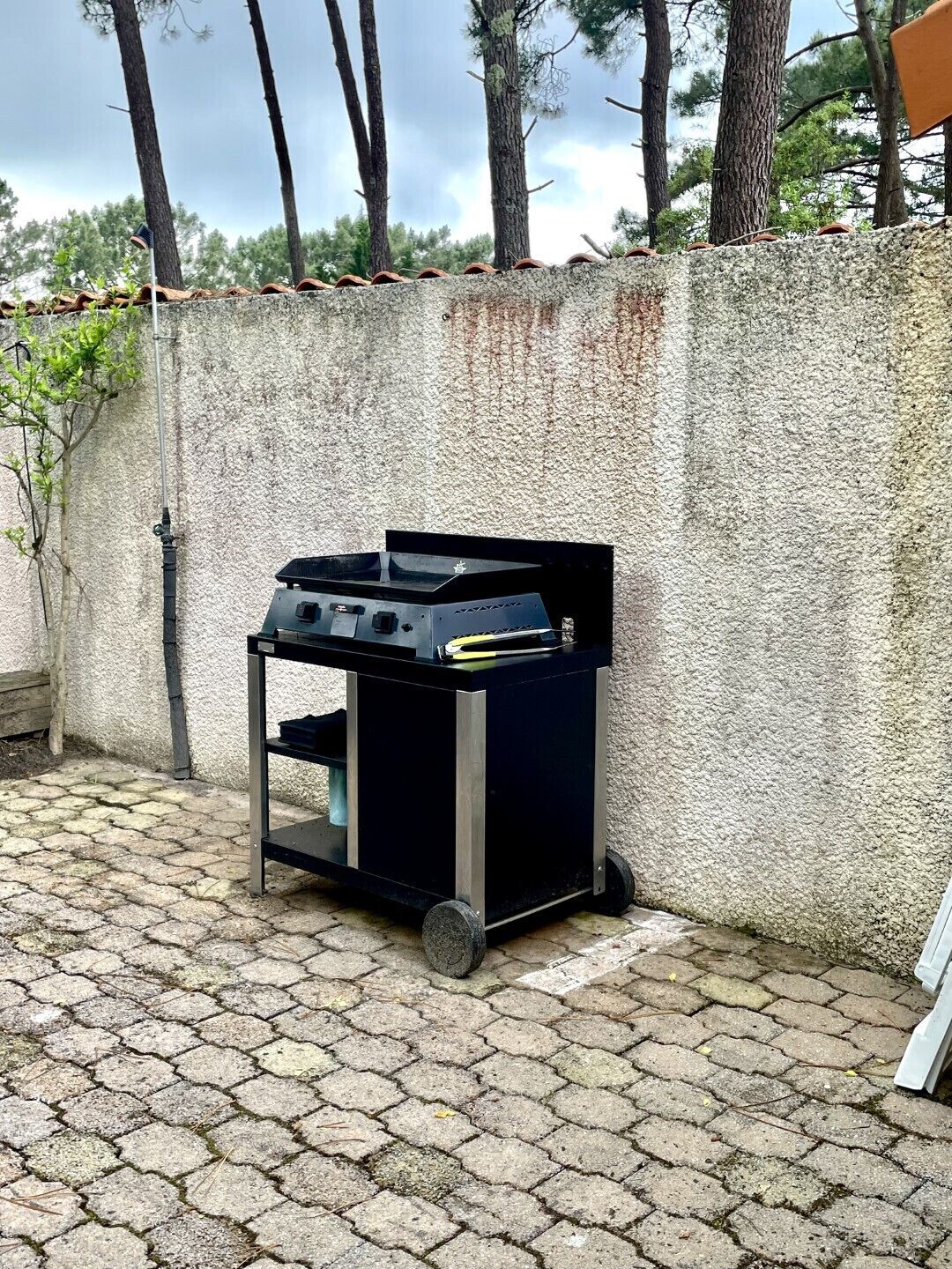 Een draagbare gasgrill met een zwart frame en wielen, geplaatst op een geplaveid terras tegen een gestructureerde muur.