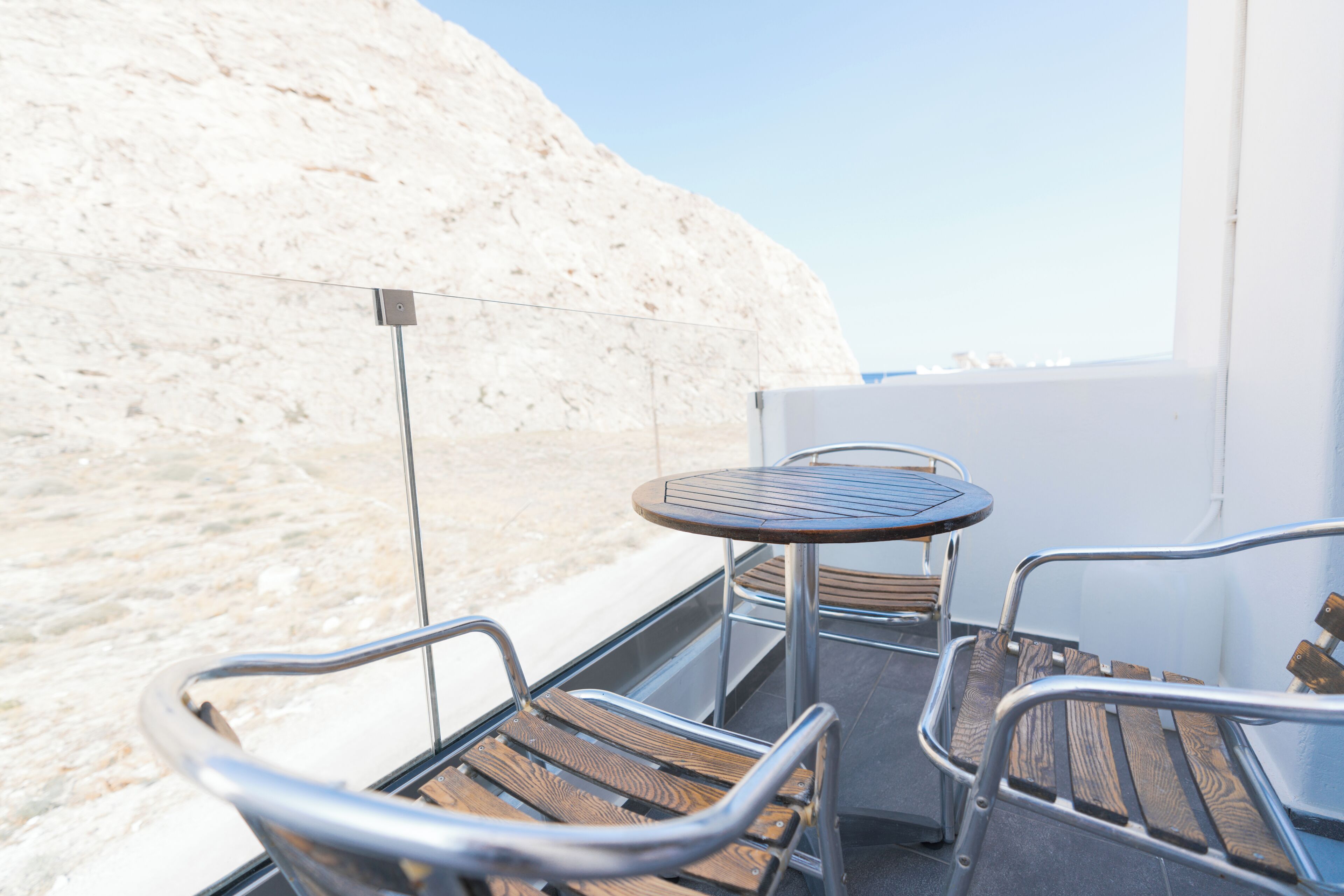 Een balkon met metalen stoelen en een kleine ronde tafel, met uitzicht op een zandstrand en de zee.