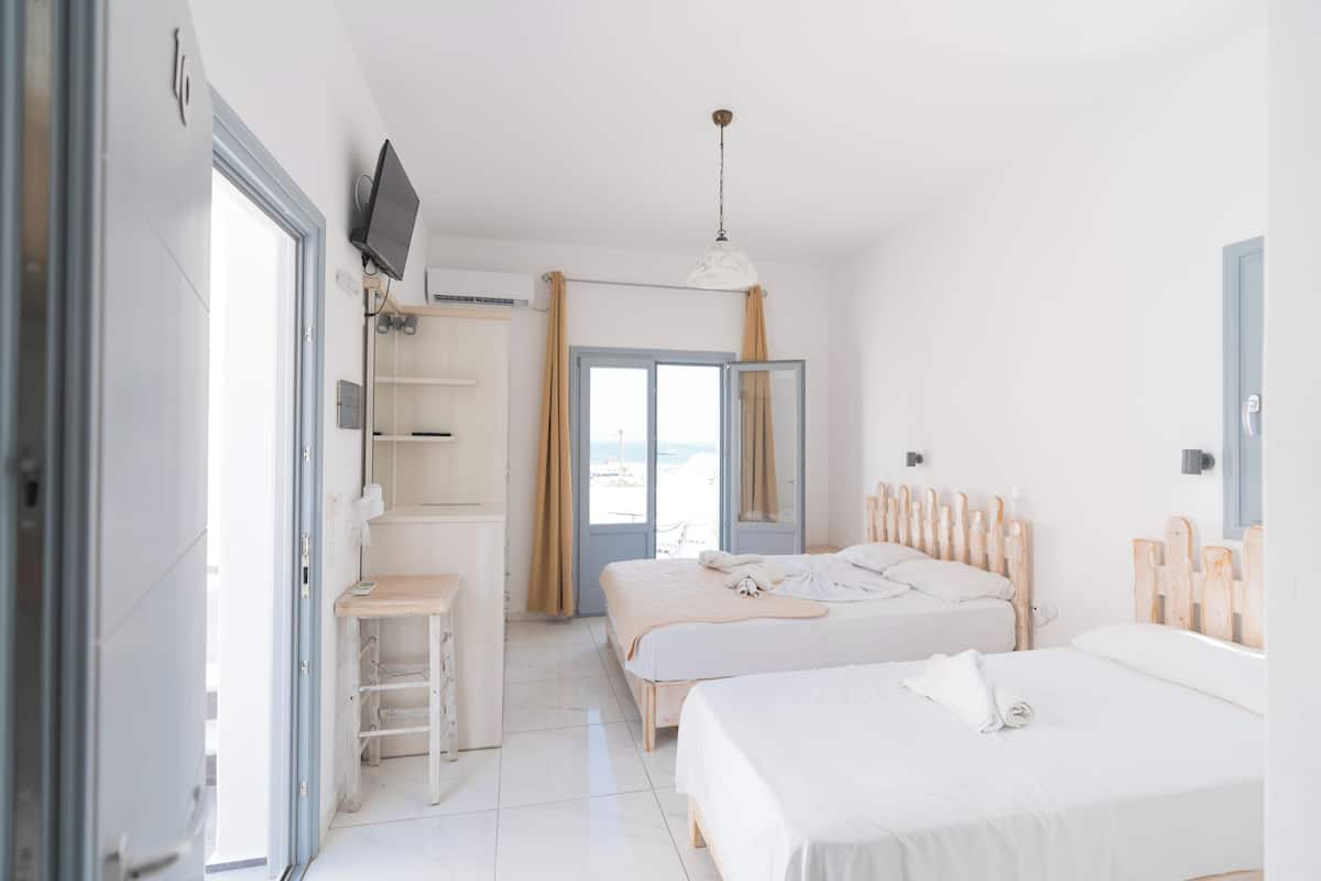 A hotel room with two beds, a TV, a desk, and a view of the sea.