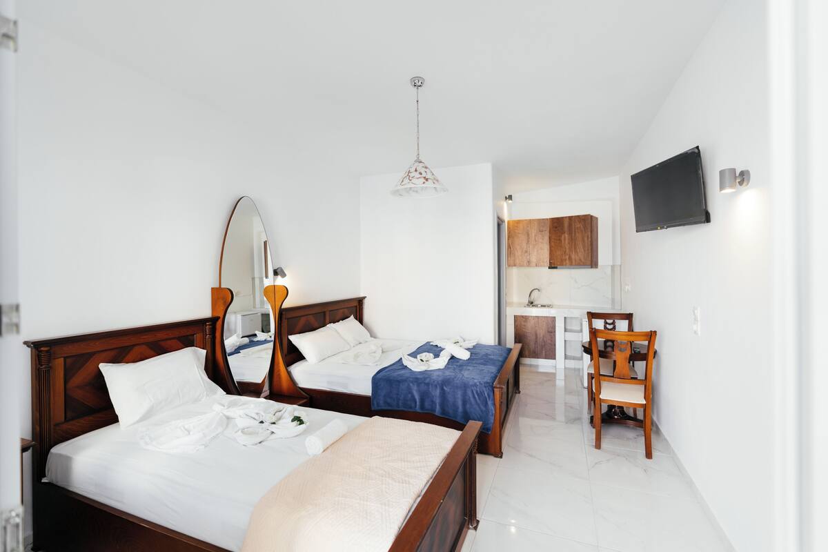 A hotel room with two beds, a wooden headboard, a large mirror, a hanging light fixture, a television, and a wooden chair.