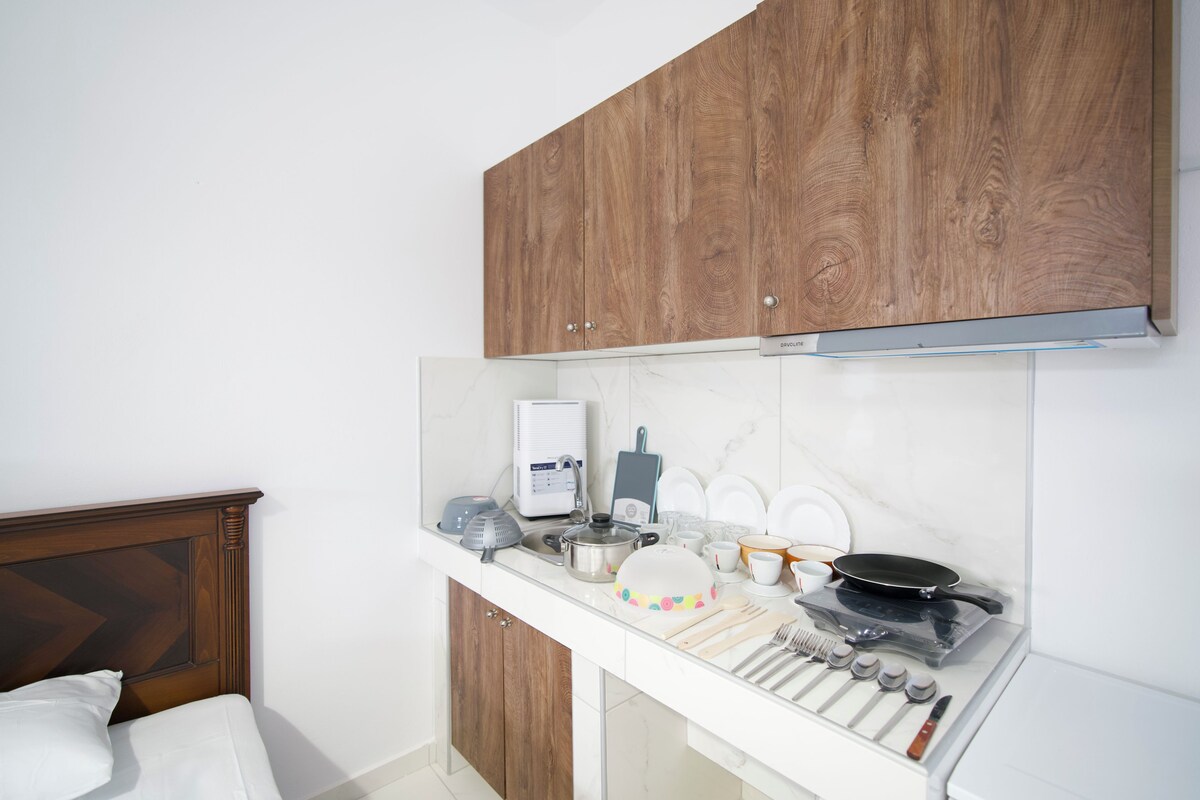 A compact kitchen with wooden cabinets, a microwave, a kettle, and various kitchen utensils.