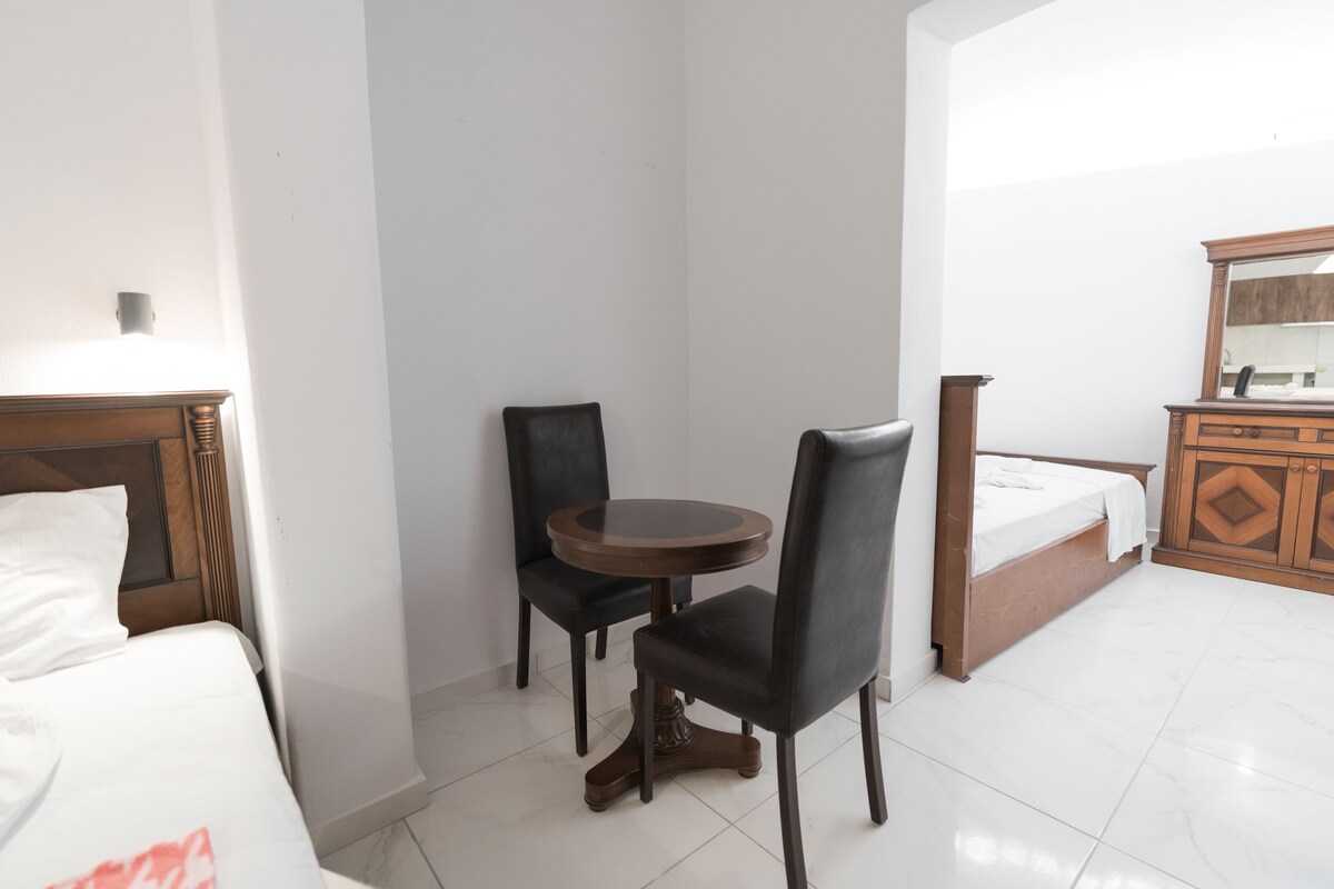 A hotel room with a bed, a small round table with two chairs, a dresser, and a mirror.