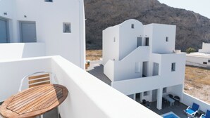 Un edificio blanco con un balcón, una mesa de madera y sillas azules.