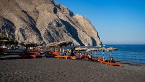 Una playa con sombrillas de paja y sillones anaranjados.
