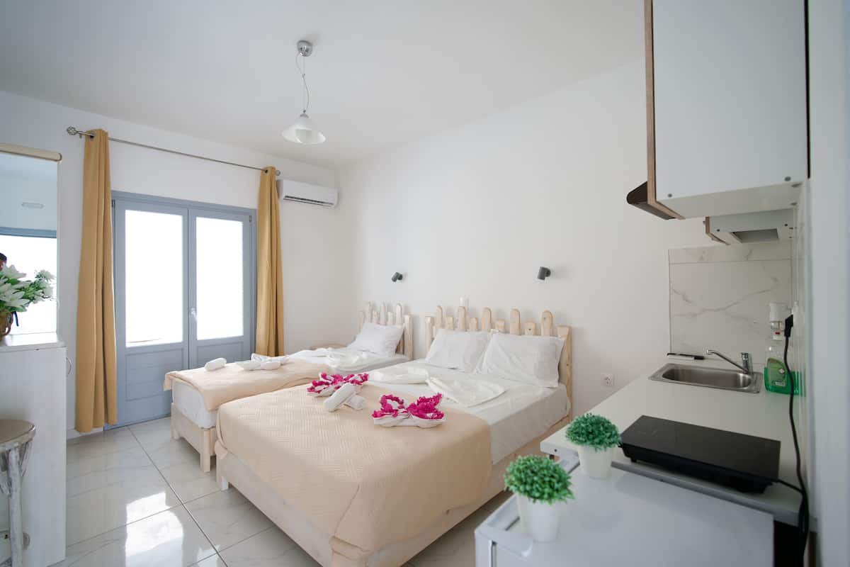 A hotel room with two beds, a small kitchenette, a bathroom with a sink, and a window with curtains.