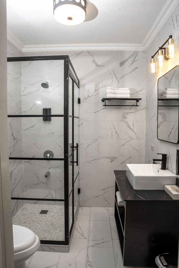 Un baño moderno con ducha de vidrio, lavamanos blanco y piso de baldosas de mármol.
