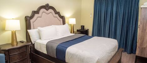 A neatly made bed with a headboard, two bedside tables with lamps, a blue curtain, and a wooden wardrobe.