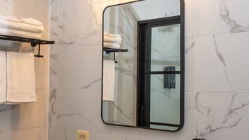 Un bagno con un lavandino bianco, un piano di lavoro nero e uno specchio con cornice nera. Asciugamani su uno stendino e un dispenser di sapone a parete.