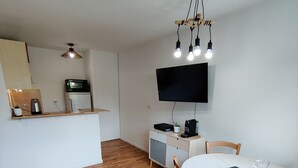 A compact living space with a kitchenette, a dining area with a table and chairs, and a mounted TV.