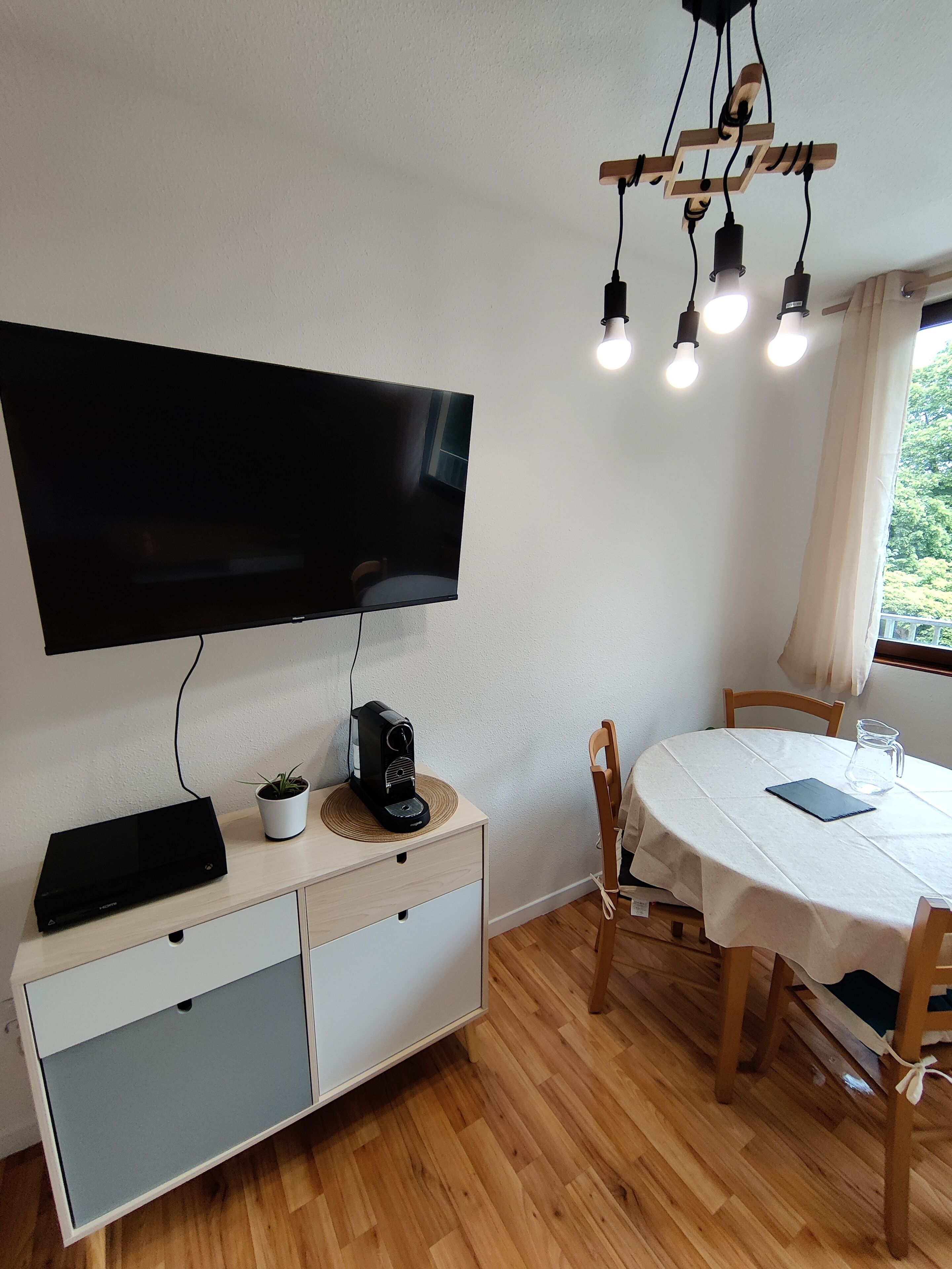 A modern living room with a flat-screen TV, a coffee maker, and a dining table with chairs.