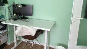 Quarto com escrivaninha, computador, cadeira e planta em vaso.