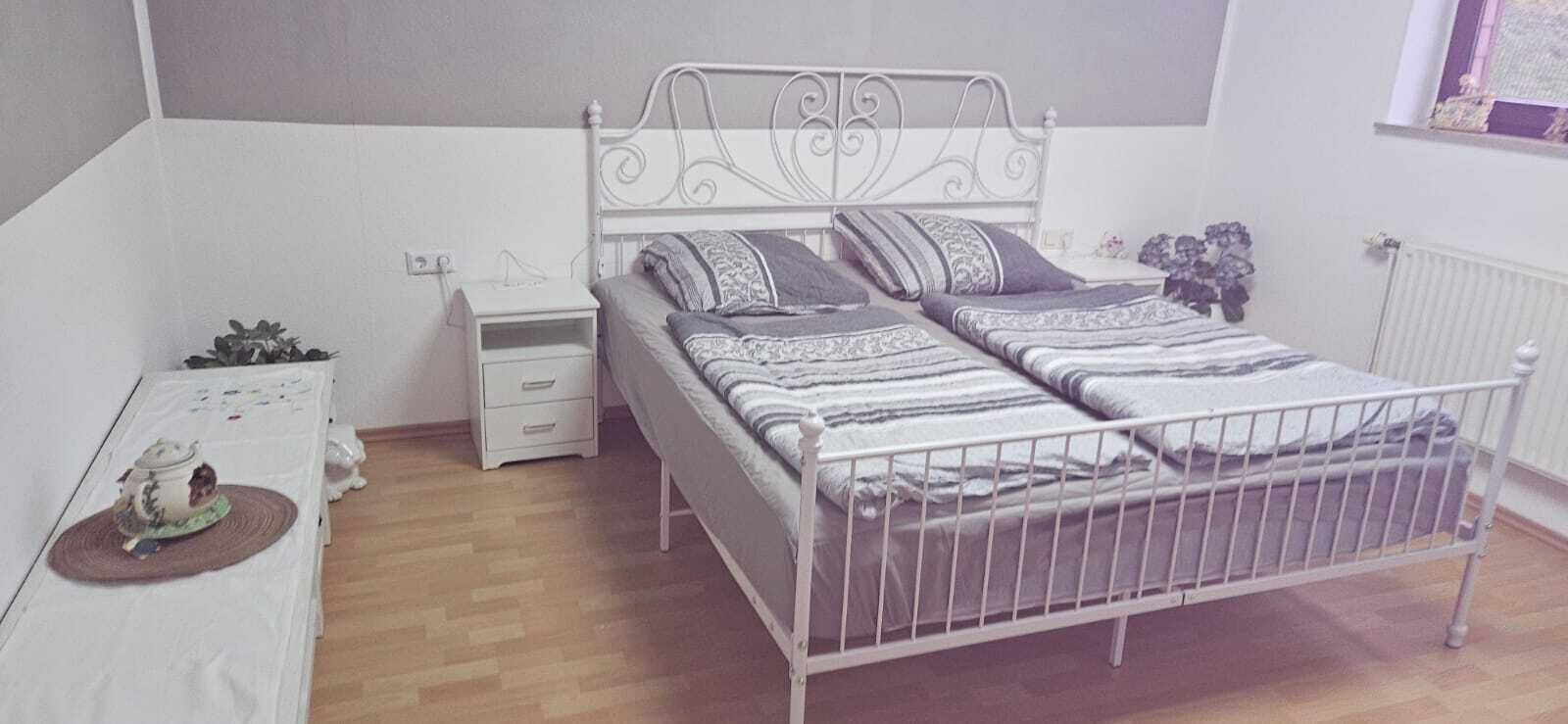 Une chambre à coucher avec un lit en métal, une table de chevet avec une lampe, une petite plante et une fenêtre donnant sur un beau paysage.