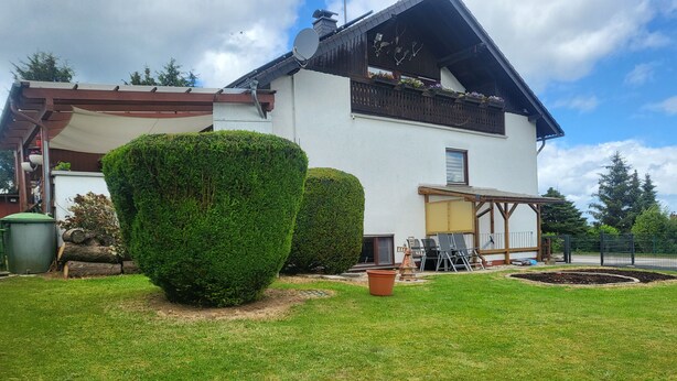 Une maison blanche avec un toit en pente, un balcon en bois orné de jardinières et une pelouse bien entretenue.