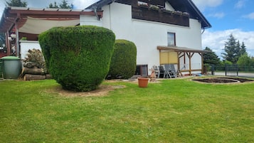 Une maison blanche avec un toit en pente, un balcon en bois orné de jardinières et une pelouse bien entretenue.