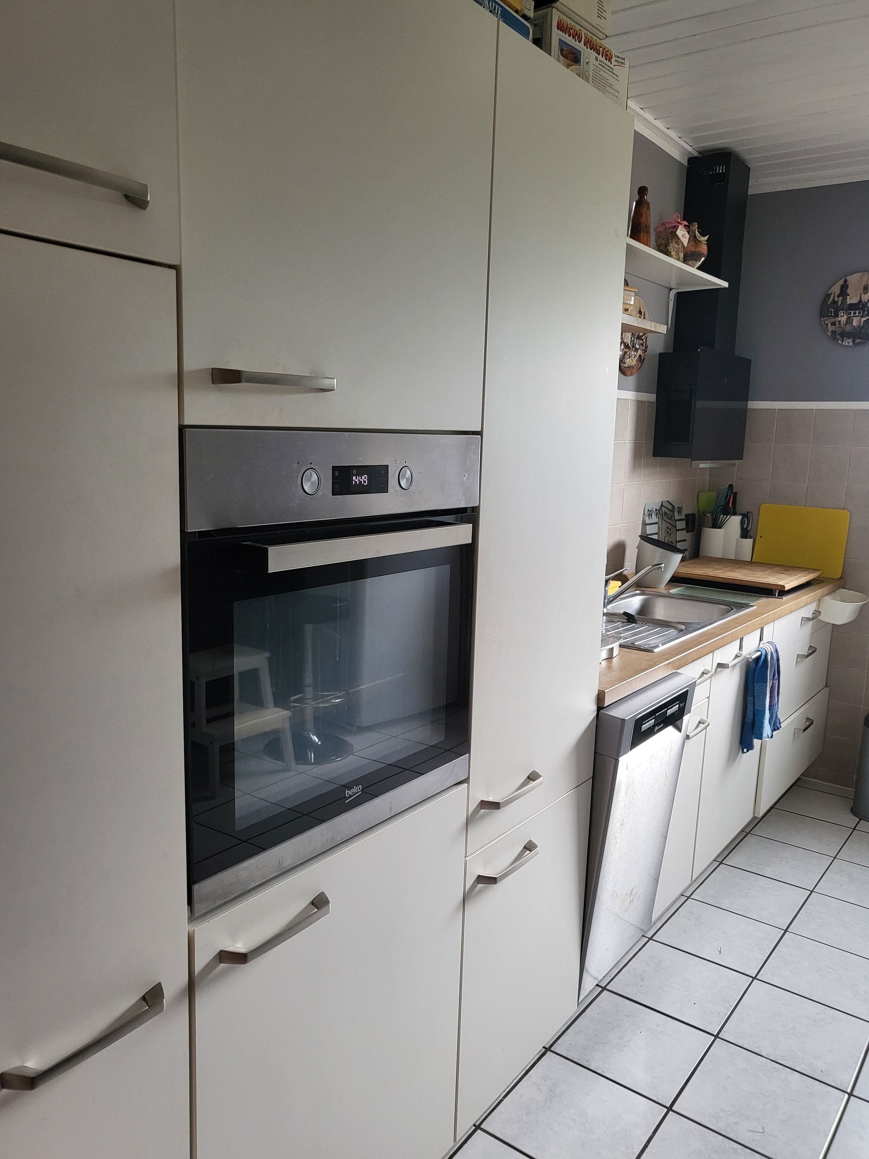 Une cuisine avec des armoires blanches, un four encastré, un évier et une planche à découper jaune.