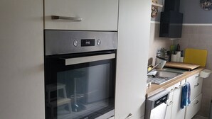 Une cuisine avec des armoires blanches, un four encastré, un évier et une planche à découper jaune.