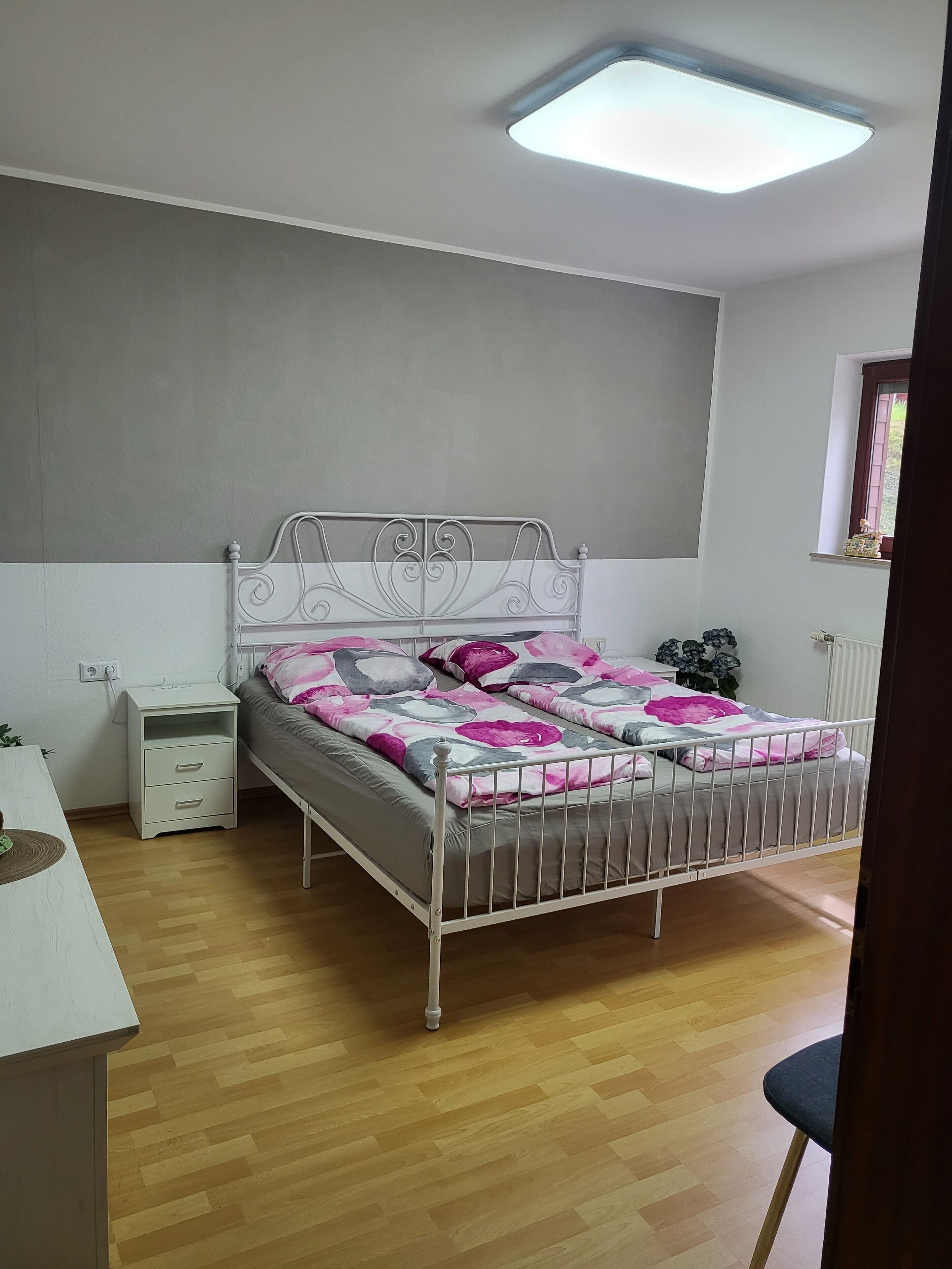 A bedroom with a bed, a nightstand, a desk, and a window.