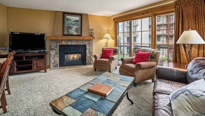 Una sala de estar con chimenea, asientos cómodos, un televisor de pantalla plana y ventanas grandes.