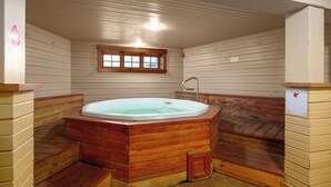 Una bañera de hidromasaje de madera con un ventanal encima, rodeada de paredes y bancos de madera.