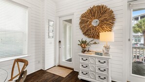 A room with white paneled walls, a wooden floor, a large wall clock, a white dresser with black handles, and a window with blinds. - Sailfish Lookout, Private Beach Access (Panama City Beach)