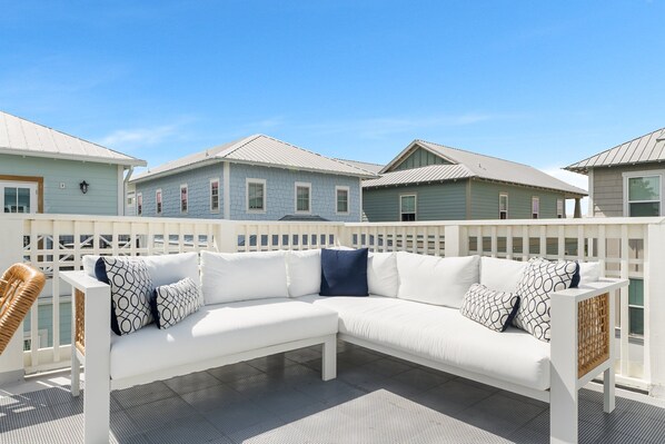 A white outdoor seating area with a woven chair, a white sofa with patterned cushions, and a view of neighboring houses. - Sailfish Lookout, Private Beach Access (Panama City Beach)