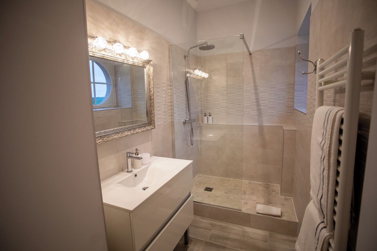 Een moderne badkamer met een wastafel, een grote spiegel, een douche en een handdoekrek.