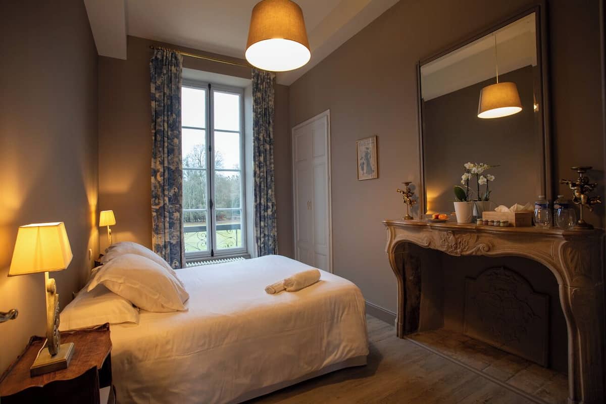 Een hotelkamer met een bed, een dressoir, een spiegel, een raam met gordijnen en een lamp.