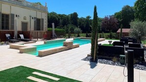 A swimming pool with a tiled deck, surrounded by a well-maintained lawn and various plants.