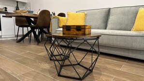A modern living room with a wooden floor, a grey sofa with yellow cushions, and a vintage suitcase on a metal table. - Tarraco Civitas ubi ver Aeternum Est. Totalmente Reformado y con Ascensor (Tarragona)