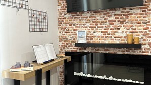 A room with a brick wall, a mounted TV, a fireplace with a stone border, and a wooden table with a book and decorative items. - Tarraco Civitas ubi ver Aeternum Est. Totalmente Reformado y con Ascensor (Tarragona)
