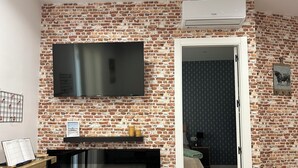A room with a brick wall, a flat-screen TV mounted above a fireplace, and a door leading to another room. - Tarraco Civitas ubi ver Aeternum Est. Totalmente Reformado y con Ascensor (Tarragona)