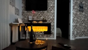 A room with a brick wall, a fireplace, a flat-screen TV mounted above it, and a table with a bottle and glasses. - Tarraco Civitas ubi ver Aeternum Est. Totalmente Reformado y con Ascensor (Tarragona)
