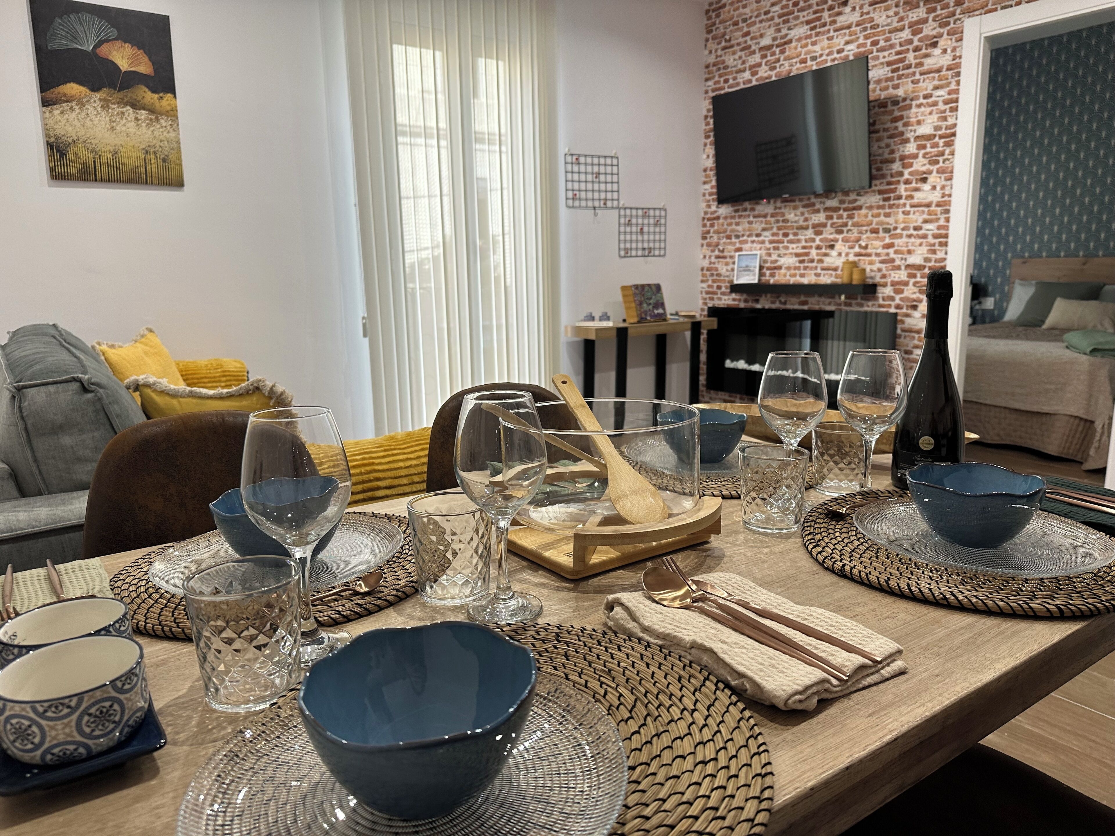 Une table à manger dressée avec de la vaisselle et des bols, une cuillère en bois et une bouteille de vin.