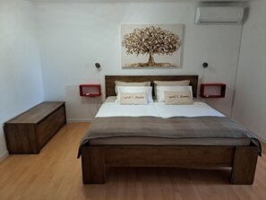 Ein Schlafzimmer mit einem hölzernen Bett, zwei Nachttischen, einer Wand-Klimaanlage und einem Baumgemälde.