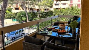 Un balcón con mobiliario de mimbre, una mesa de comedor con platos, vasos y una cesta de pan.