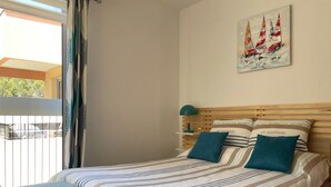 Un dormitorio con cama, almohadas, una mesita de noche, una lámpara y un cuadro en la pared.