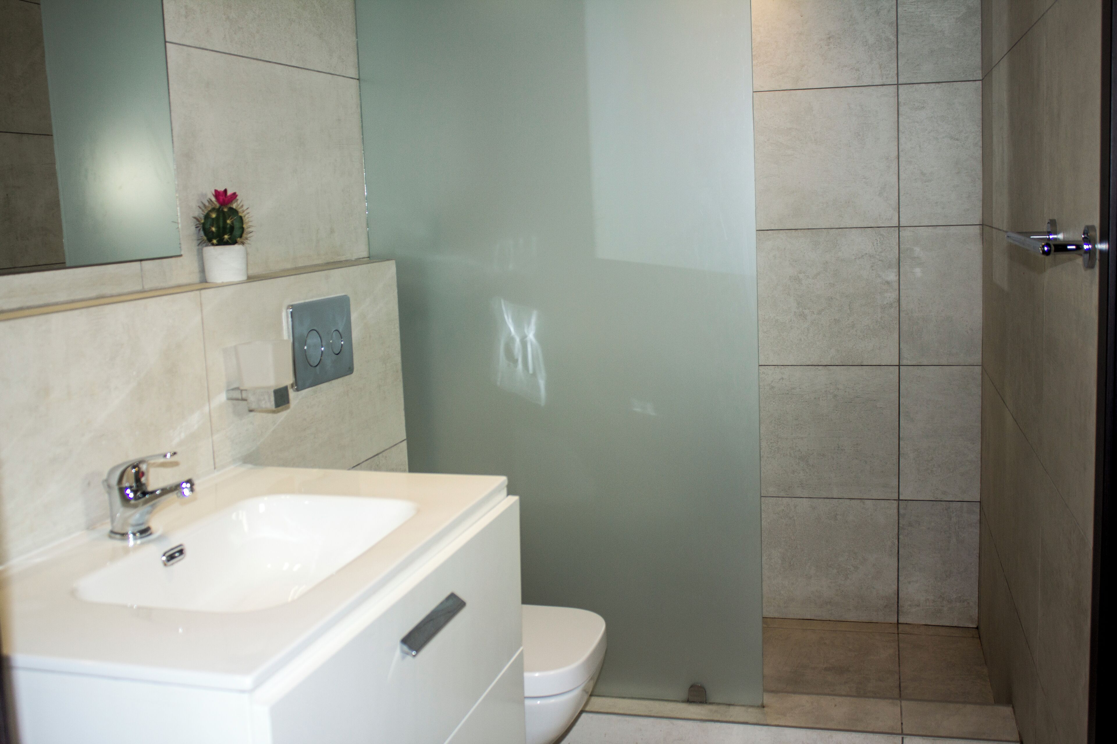 Un baño moderno con un lavabo blanco, un inodoro y una cabina de ducha con mampara de vidrio.