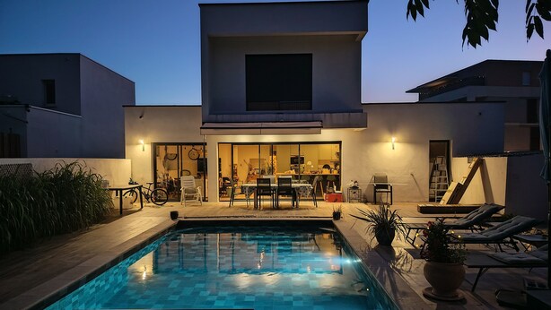 A modern house with a swimming pool, outdoor seating, and a visible kitchen area.